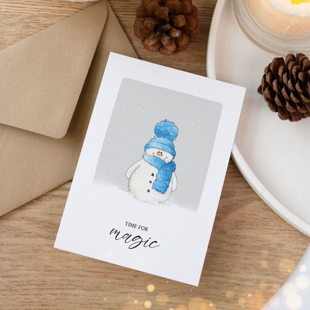 Künstlerische Weihnachtskarte mit handgemaltem Schneemann, blauer Schal und Mütze, verschneiter Hintergrund – Aquarell-Klappkarte für den Winter.