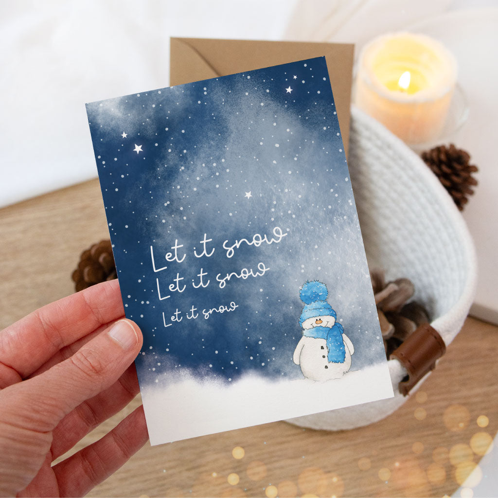 Klappkarte mit Schneemann und dem Schriftzug „Let it snow“ wird in einer Hand präsentiert – liebevoll gestaltete Aquarell-Weihnachtskarte für persönliche Grüße.