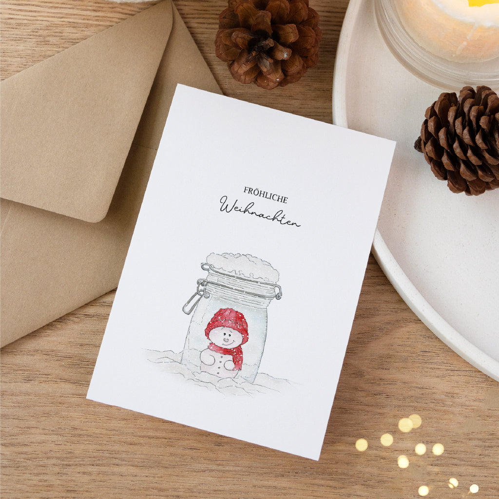 Hochwertige Postkarte mit Schneemann im Glas Aquarell Motiv angelehnt an einen Teller mit weihnachtlicher Deko.
