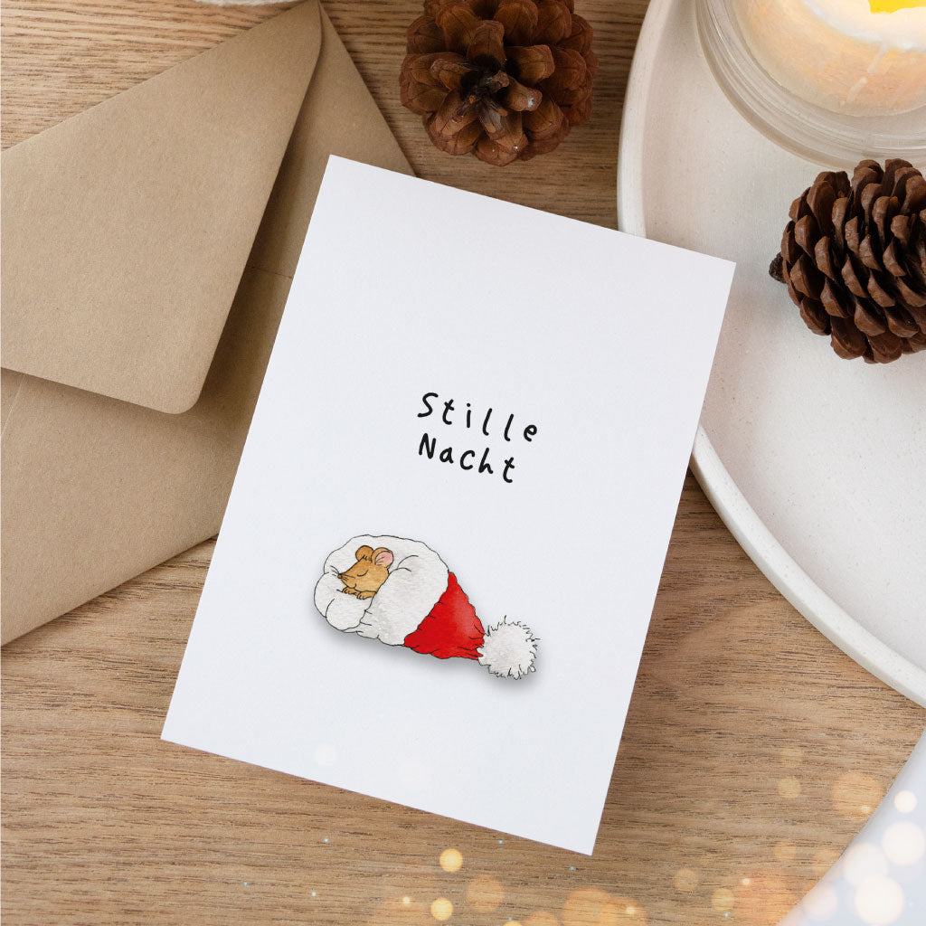 Postkarte „Stille Nacht“ mit handgemaltem Aquarell einer Maus in einer Nikolausmütze, festlich dekoriert mit Tannenzapfen, Kerze und naturfarbenem Umschlag.