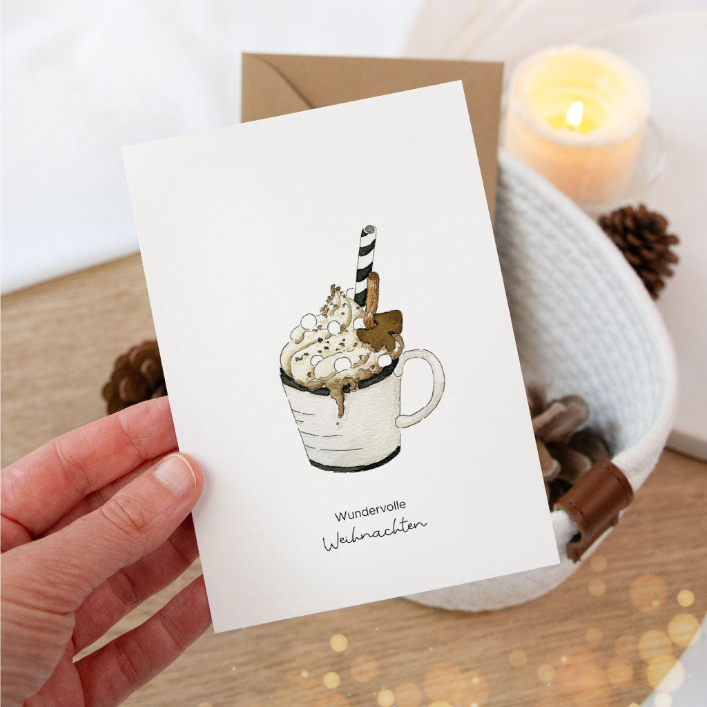 Nahaufnahme der Postkarte mit Aquarell-Tasse heißer Schokolade in der Hand gehalten, ideal als liebevolle Weihnachtskarte oder zum Verpacken von Weihnachtsgeschenken.