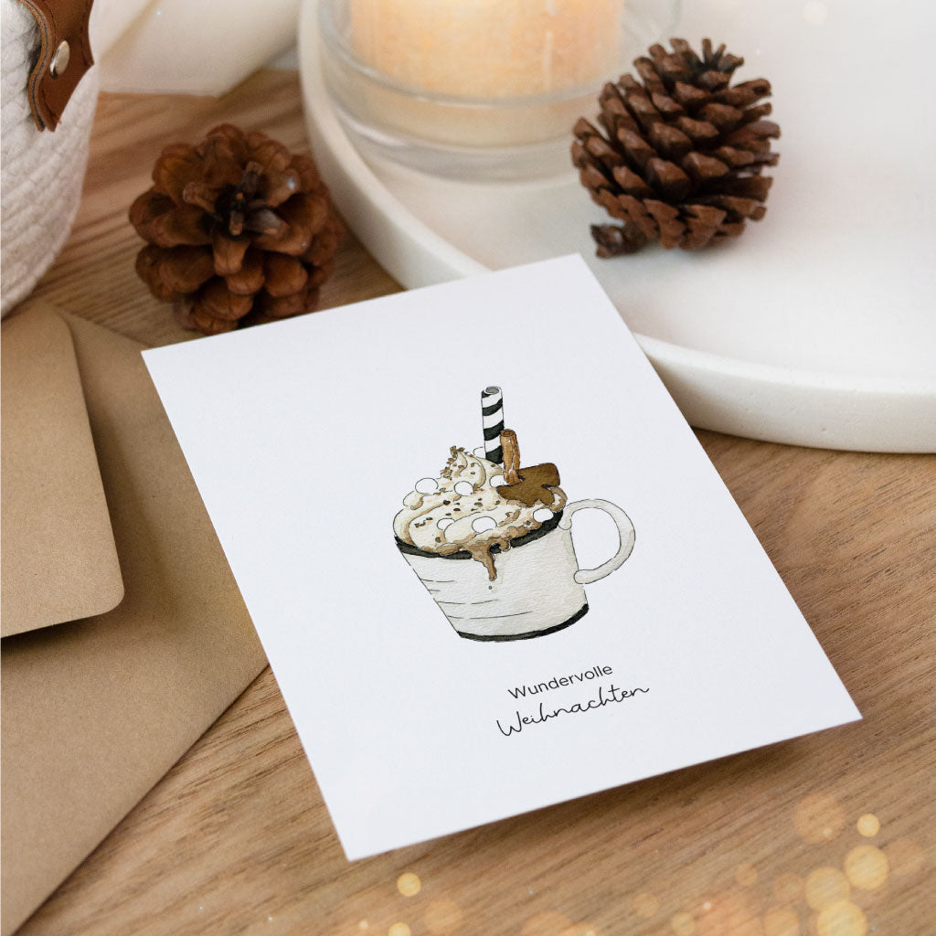 Weihnachtlich inszenierte Postkarte mit Aquarellmotiv einer heißen Schokolade, daneben Tannenzapfen, Kerze und naturfarbener Umschlag – perfekt für festliche Grüße.