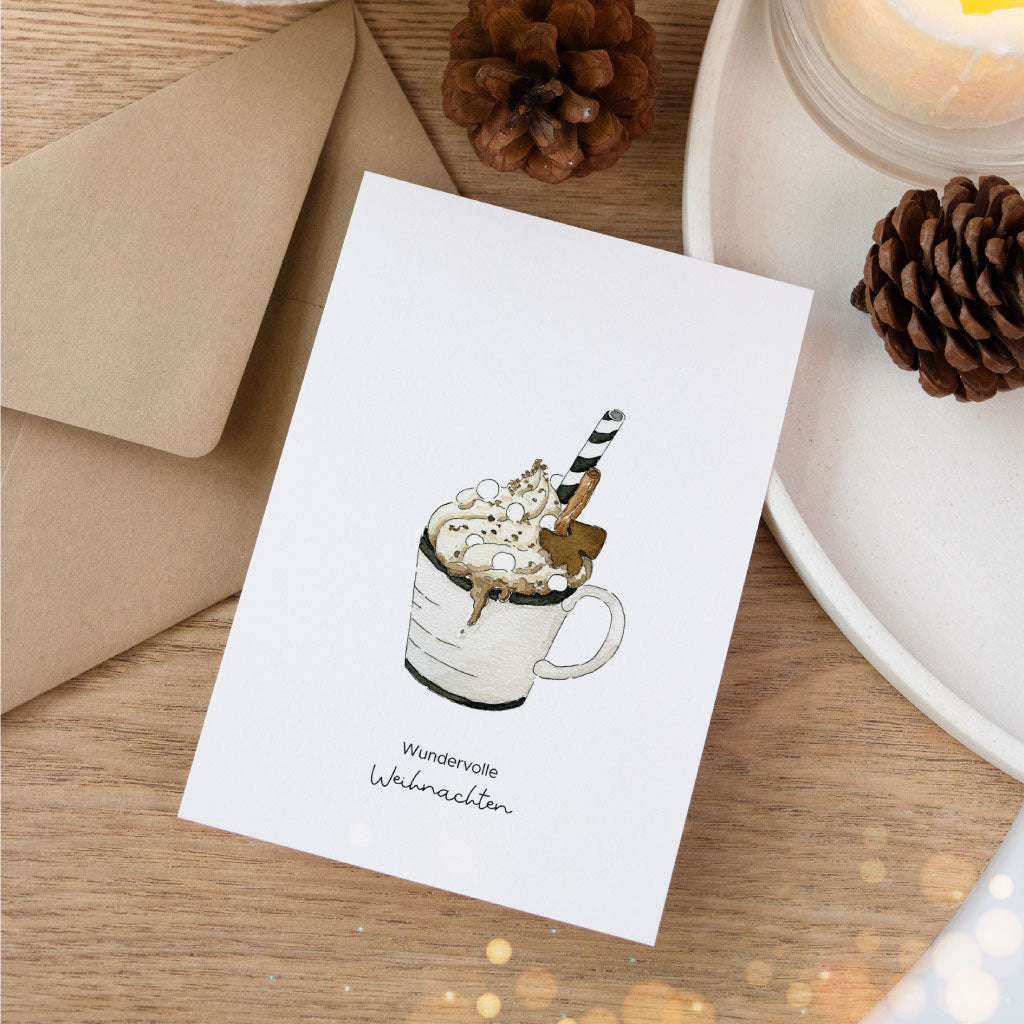 Stimmungsvolle Szene mit Weihnachtskarte im Aquarellstil, die eine Tasse heiße Schokolade zeigt, kombiniert mit Kerzendeko und braunem Umschlag auf Holzuntergrund.