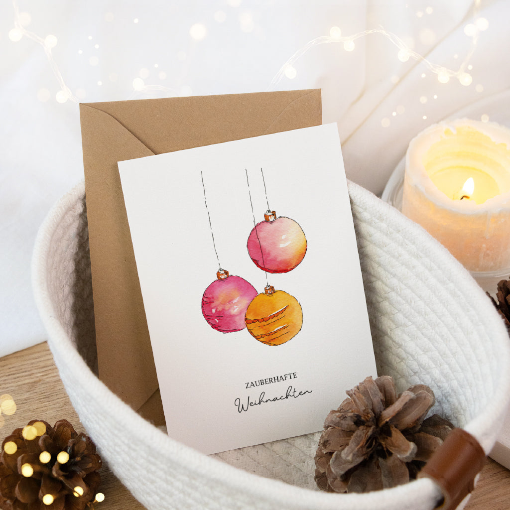 Weihnachtskarte mit Aquarell Motiv dekoriert in einem hellen Körbchen mit Tannenzapfen und einer leuchtenden Kerze.