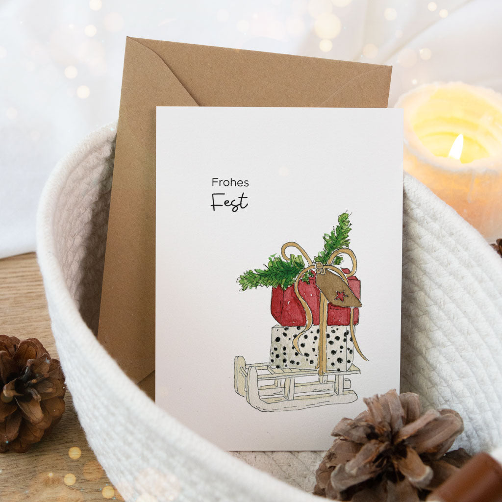 Winterliche Grußkarte mit Aquarellmotiv: Geschenke auf einem Schlitten und dem Spruch „Frohes Fest“, liebevoll dekoriert – Teil des Weihnachtskarten Sets.