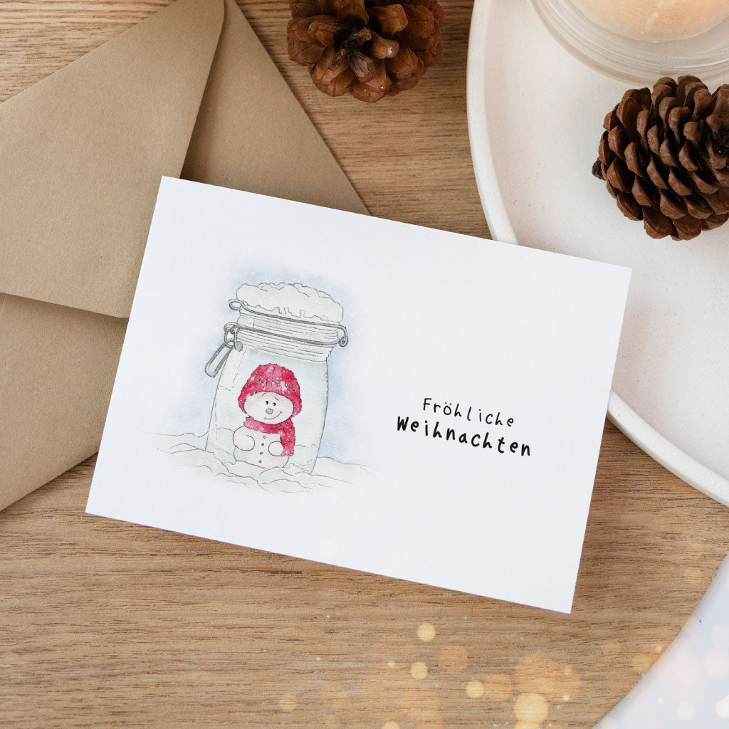 Handgemalte Grußkarte mit Schneemann in einem Einmachglas und dem Schriftzug „Fröhliche Weihnachten“ – ideal für kreative Weihnachtsgeschenke und winterliche Post.