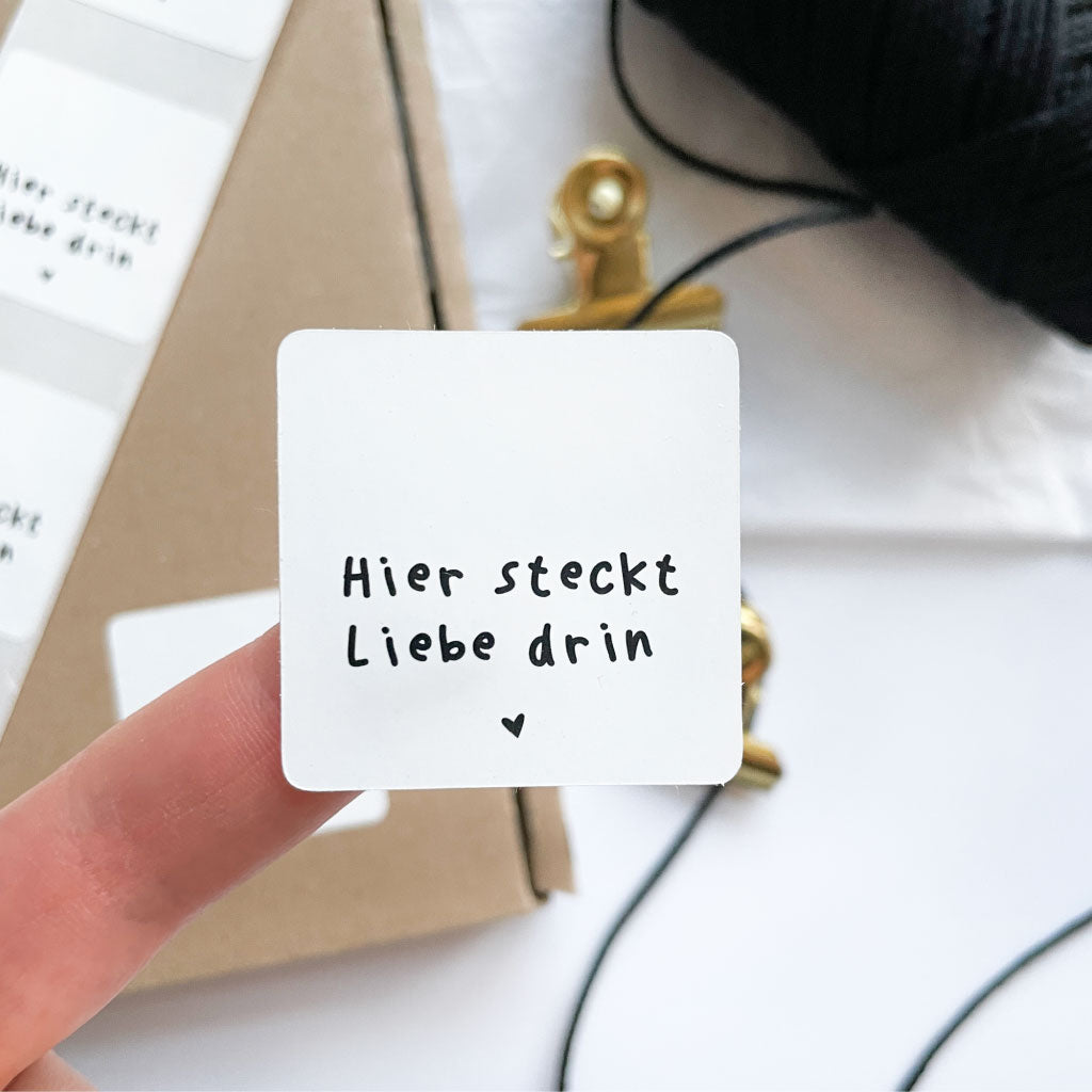 Sticker "Hier steckt Liebe drin" klebt auf Finger zum Größenvergleich