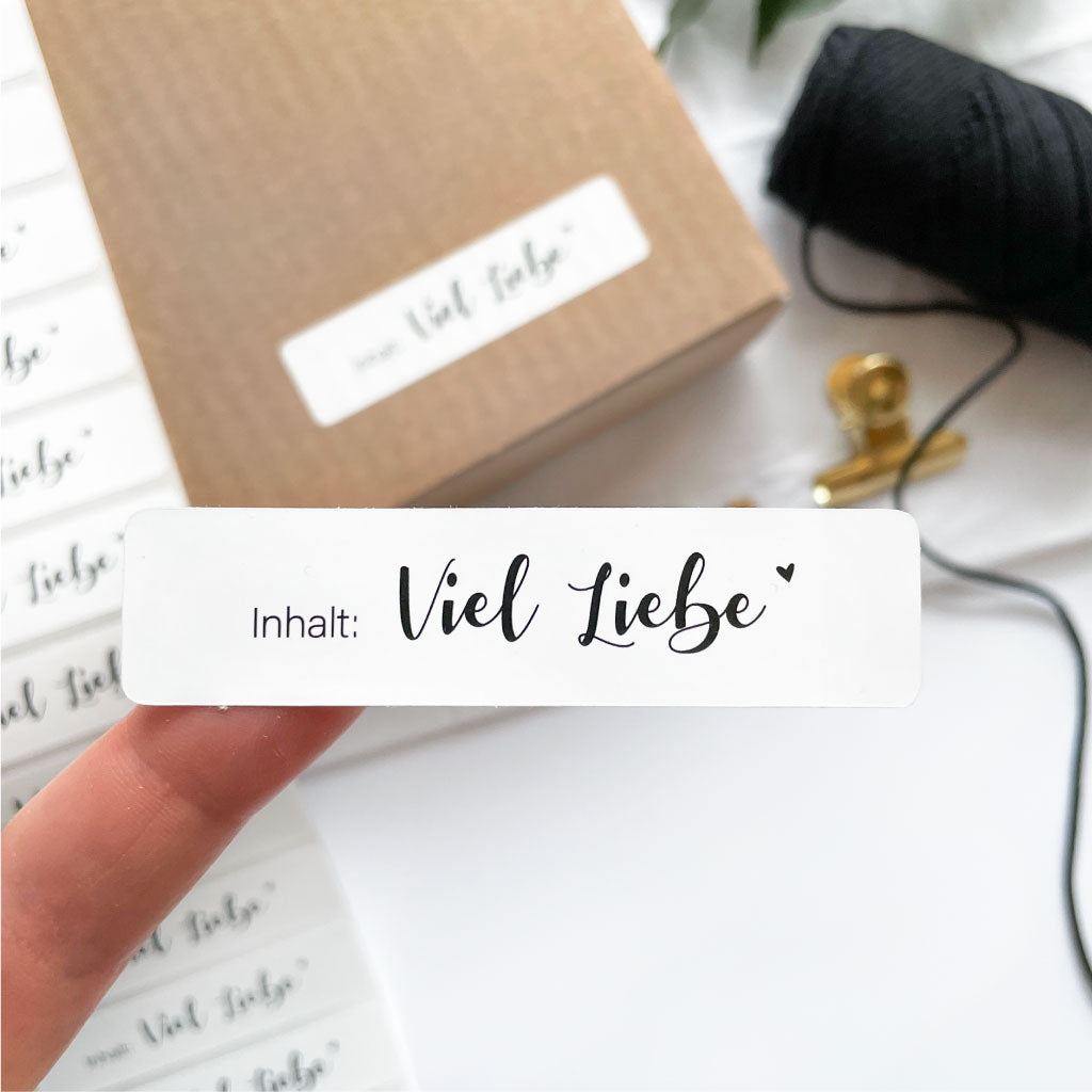 Sticker mit Text "Inhalt: Viel Liebe" klebt zum Größenvergleich auf Finger