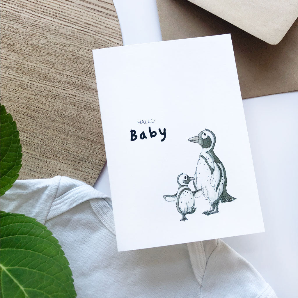 Klappkarte mit Pinguin Aquarell Motiv liegt auf weißem Baby Body