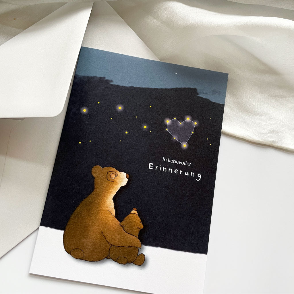 Kondolenzkarte mit Bären und Himmelsmotiv liegt neben grauem Kuvert