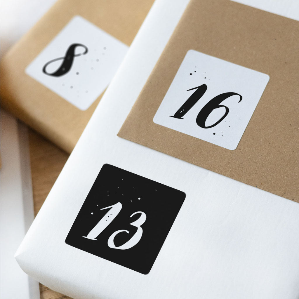 Adventskalender Zahlen Sticker auf kleinen weißen und Kraftpapier Geschenken und Kuverts, Zahlen mit weißen und schwarzen Hintergründen und kleinen Sternchen und Punkten