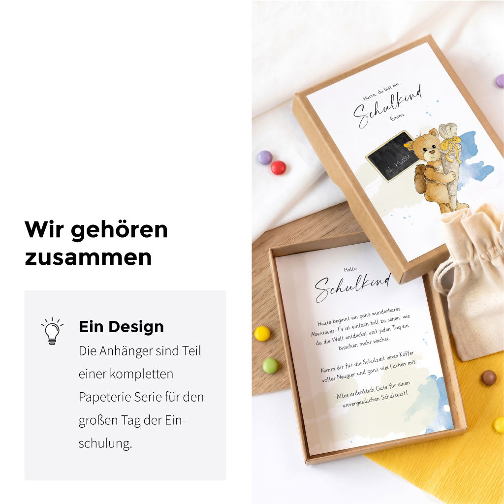 Geöffnete Geschenkschachtel zur Einschulung neben einem Anhänger mit Teddy Aquarell Motiv für eine einheitliche Deko.
