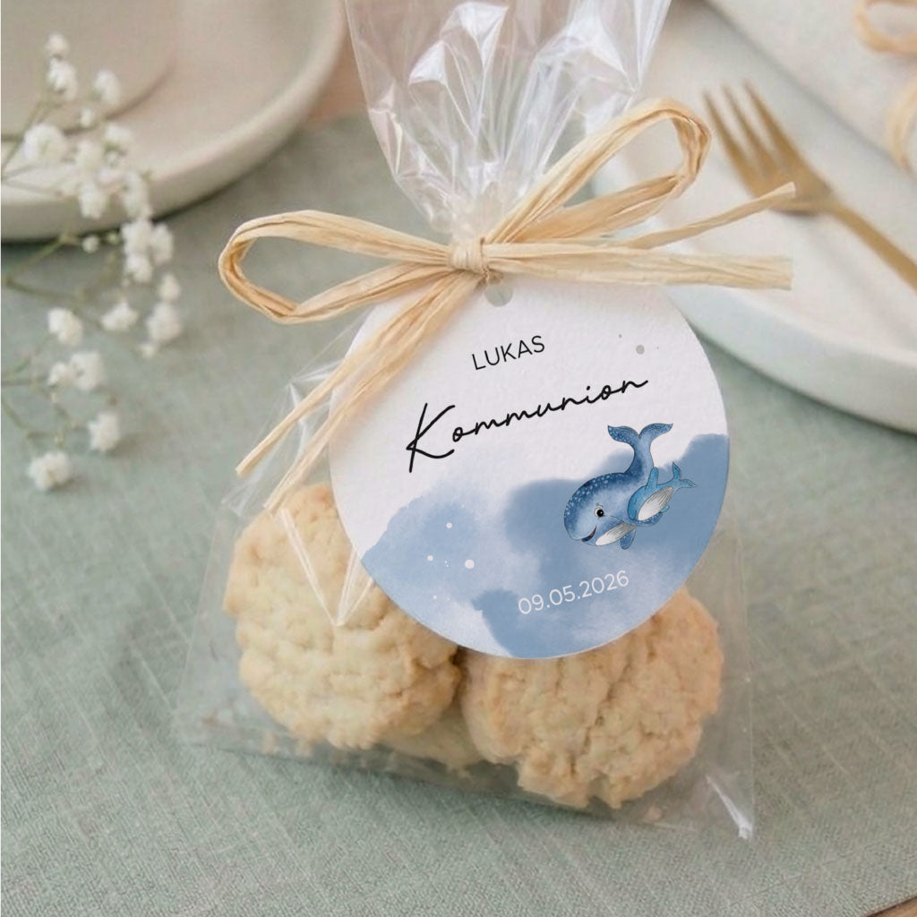 Personalisierter Anhänger zur Kommunion an einem Gastgeschenk mit Keksen und einem blauen Wal Aquarell Motiv.