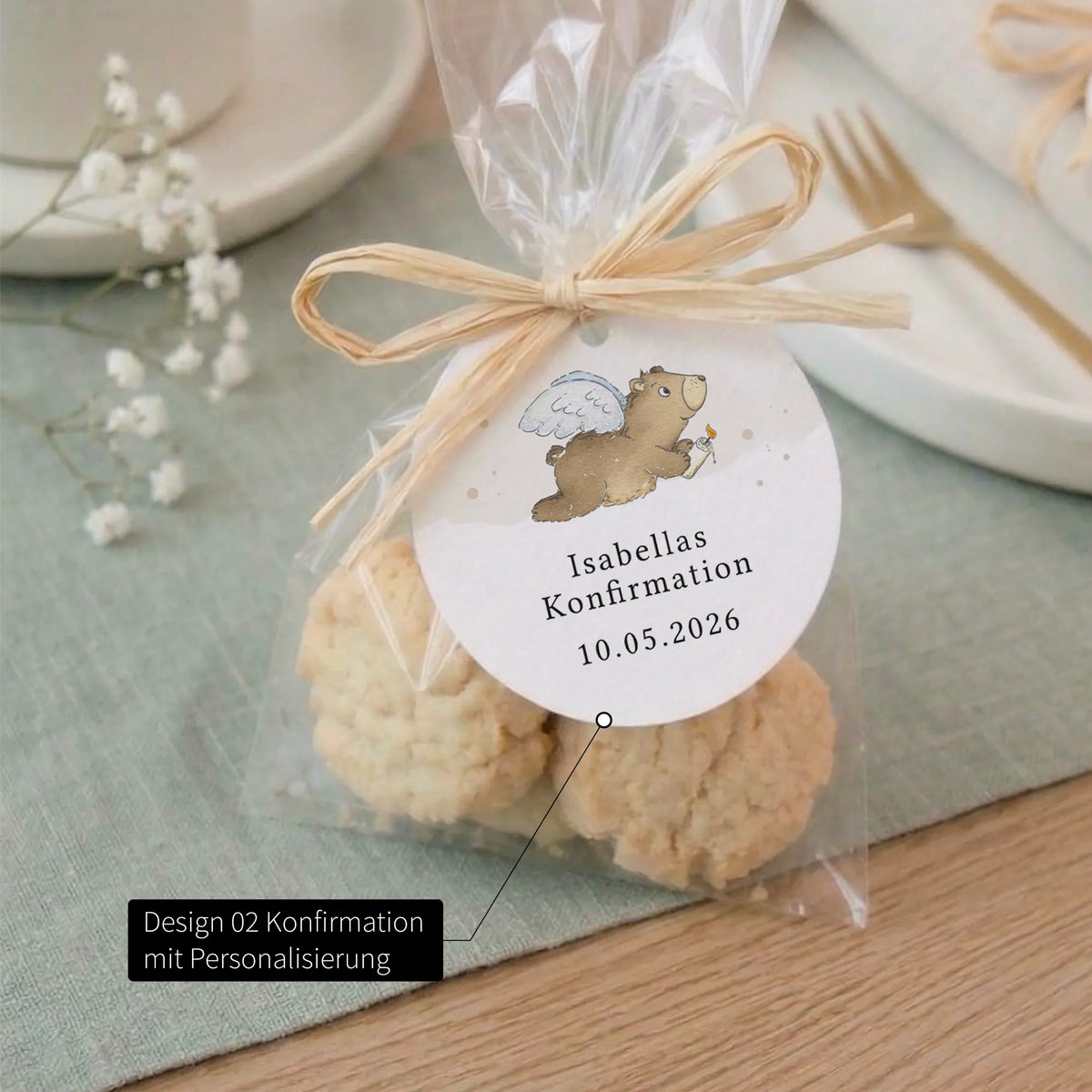 Runder Anhänger zur Konfirmation mit Aquarell Motiv Engelbär und Aufschrift Isabellas Konfirmation 10.05.2026 an Kekstüte mit Raffiaband.
