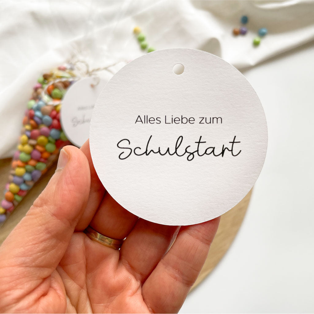 Anhänger wird in Hand gehalten, bunte Schokolinsen als Hintergrund