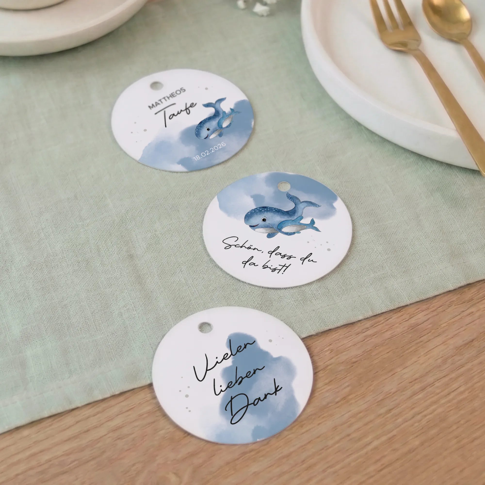 Drei runde Taufe Anhänger mit Aquarell Motiv Wal auf grünem Tischtuch: Design 01 mit Name und Datum, Design 02 Schön dass du da bist, Design 03 Vielen lieben Dank
