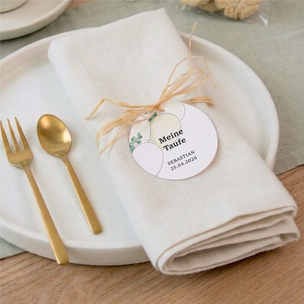 Tischdeko zur Taufe mit einem personalisierten Anhänger an einer weißen Serviette dekoriert mit goldenem Besteck.