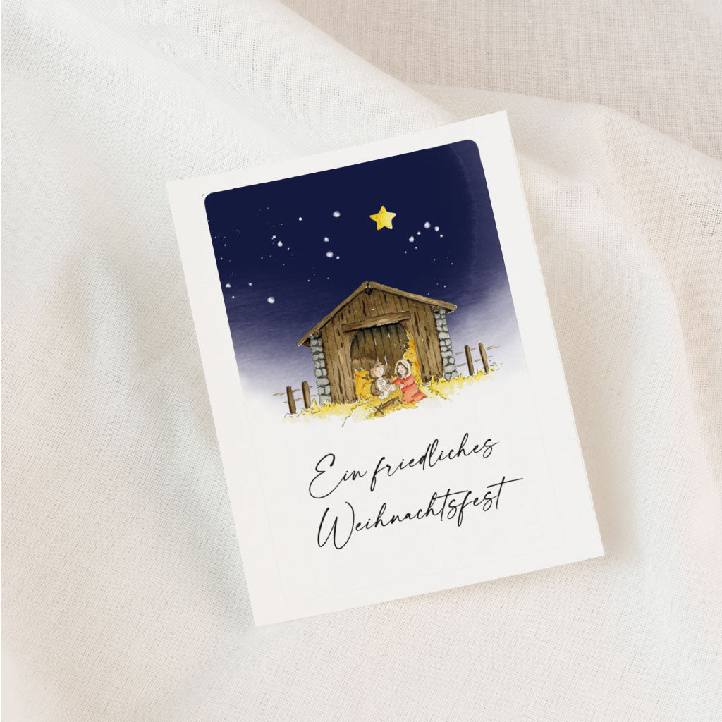 Weihnachtsaufkleber mit Aquarell-Krippenszene und Sternenhimmel auf weißem Stoff – ein ruhiger, handgemalter Sticker für Grablichter, besonders für Sternenkinder geeignet.