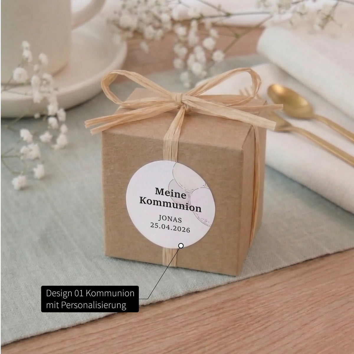 Kraftpapier-Geschenkbox mit Bast-Schleife und rundem Kommunion-Aufkleber mit Aquarell Motiv, personalisiert mit Name und Datum
