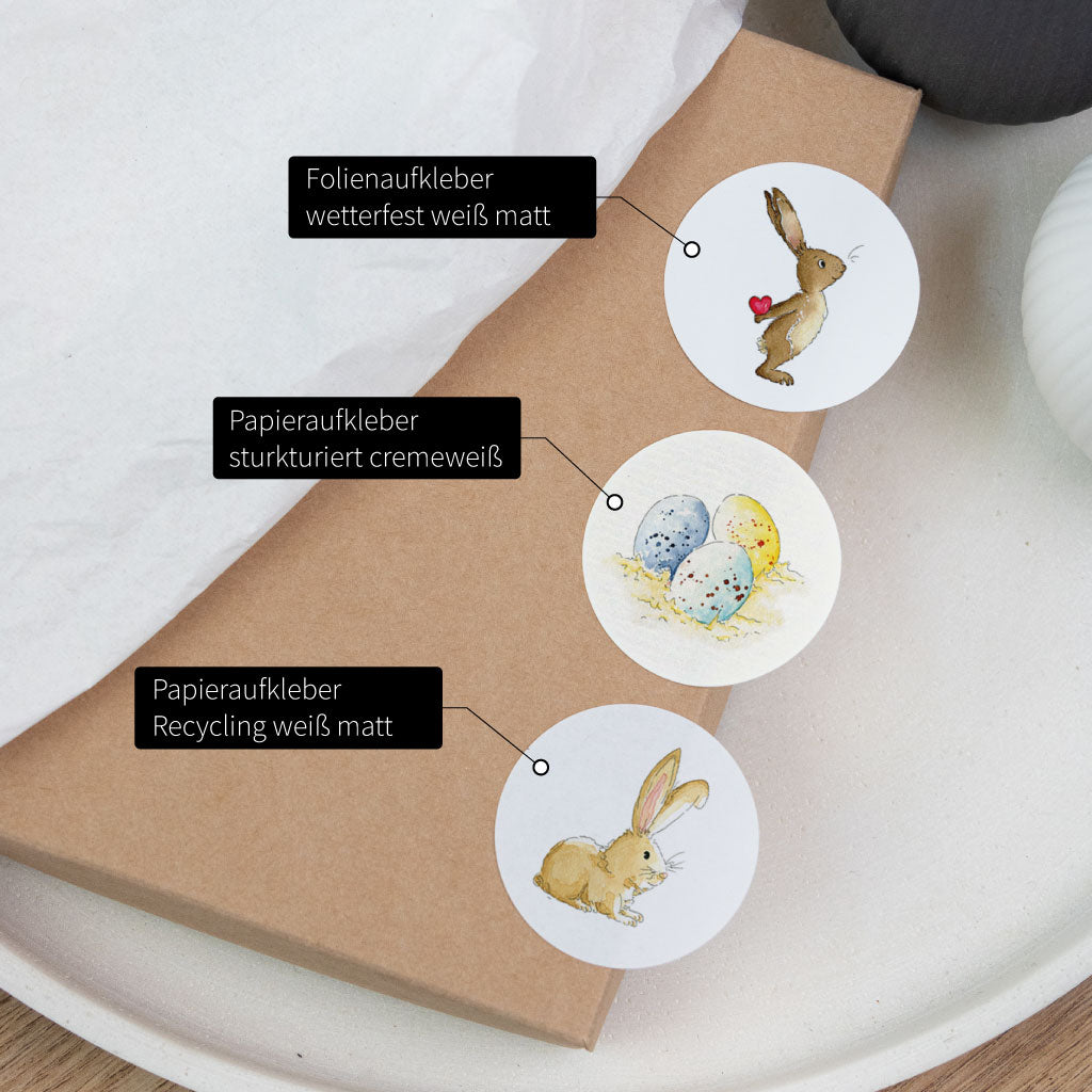 Übersicht: verschiedene Aufkleber Materialien zur Auswahl, runde Aquarell-Sticker mit Osterhase und Ostereiern auf Geschenkbox.
