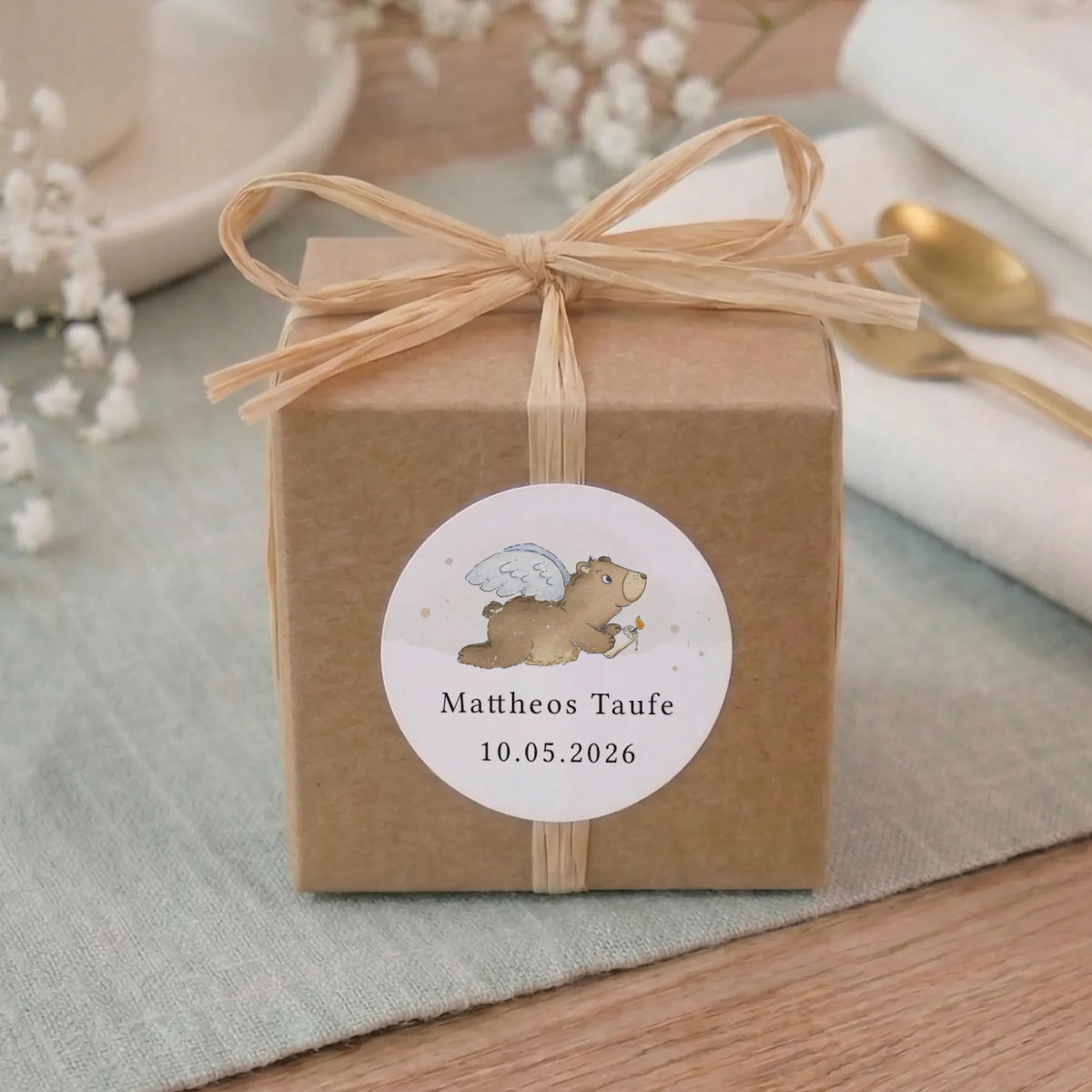 Personalisierter runder Taufe Aufkleber mit Aquarell Motiv Engelbär, Name und Datum auf Kraftpapier-Geschenkbox mit Bast-Schleife