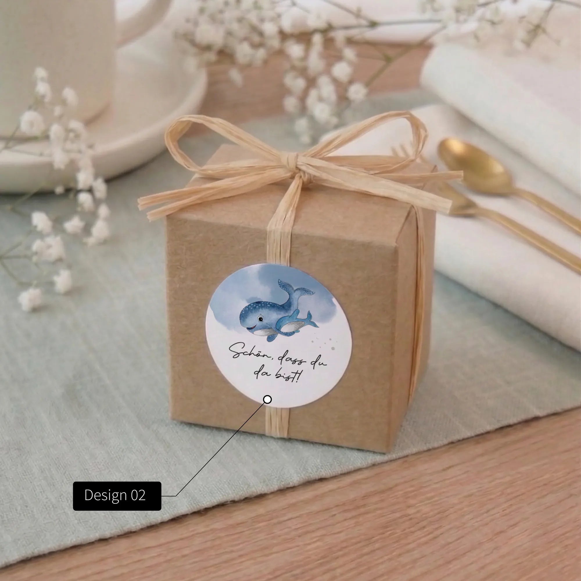 Runder Taufe Aufkleber Design 02 mit Aquarell Motiv blauem Wal und Aufschrift Schön dass du da bist auf Kraftpapier-Geschenkbox mit Bast-Schleife