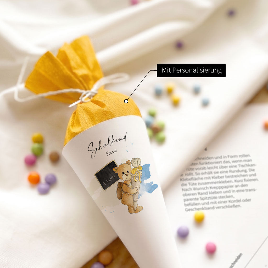 Personalisierte Mini Schultüte mit dem Namen Emma und handgemaltem Teddy Aquarell Motiv gefüllt mit gelbem Papier.