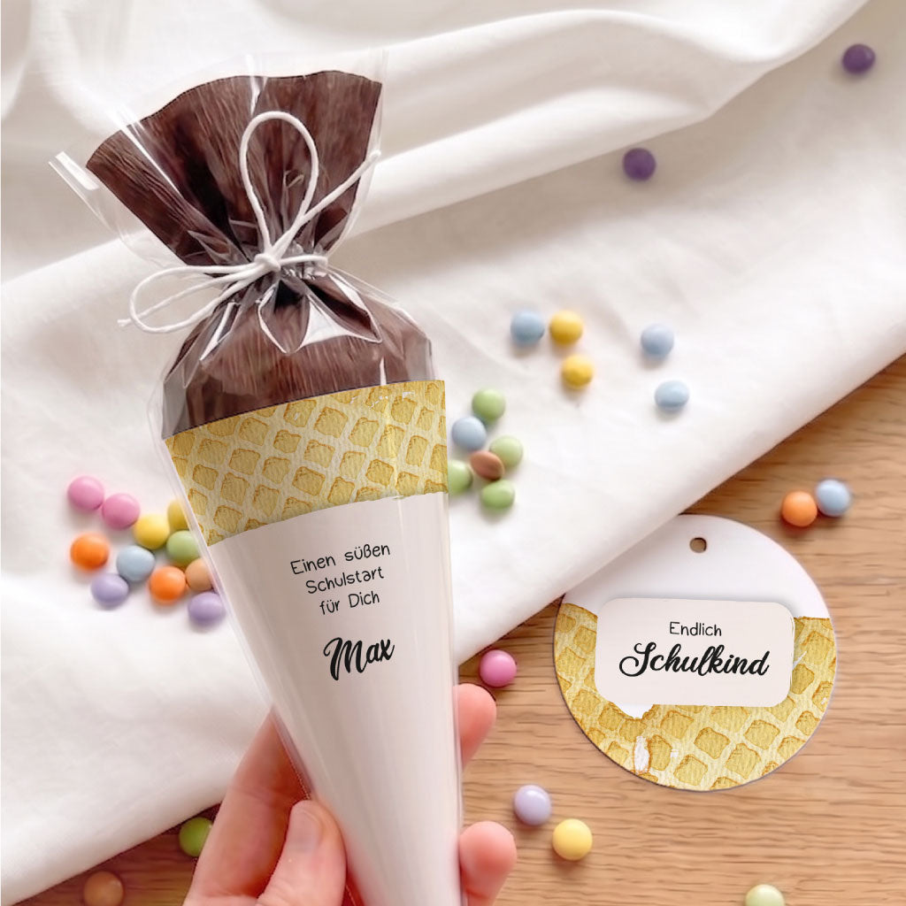 Hand hält kleine Schultüte mit Eiswaffel Aquarell Motiv. Runder Anhänger Endlich Schulkind für die Einschulung.