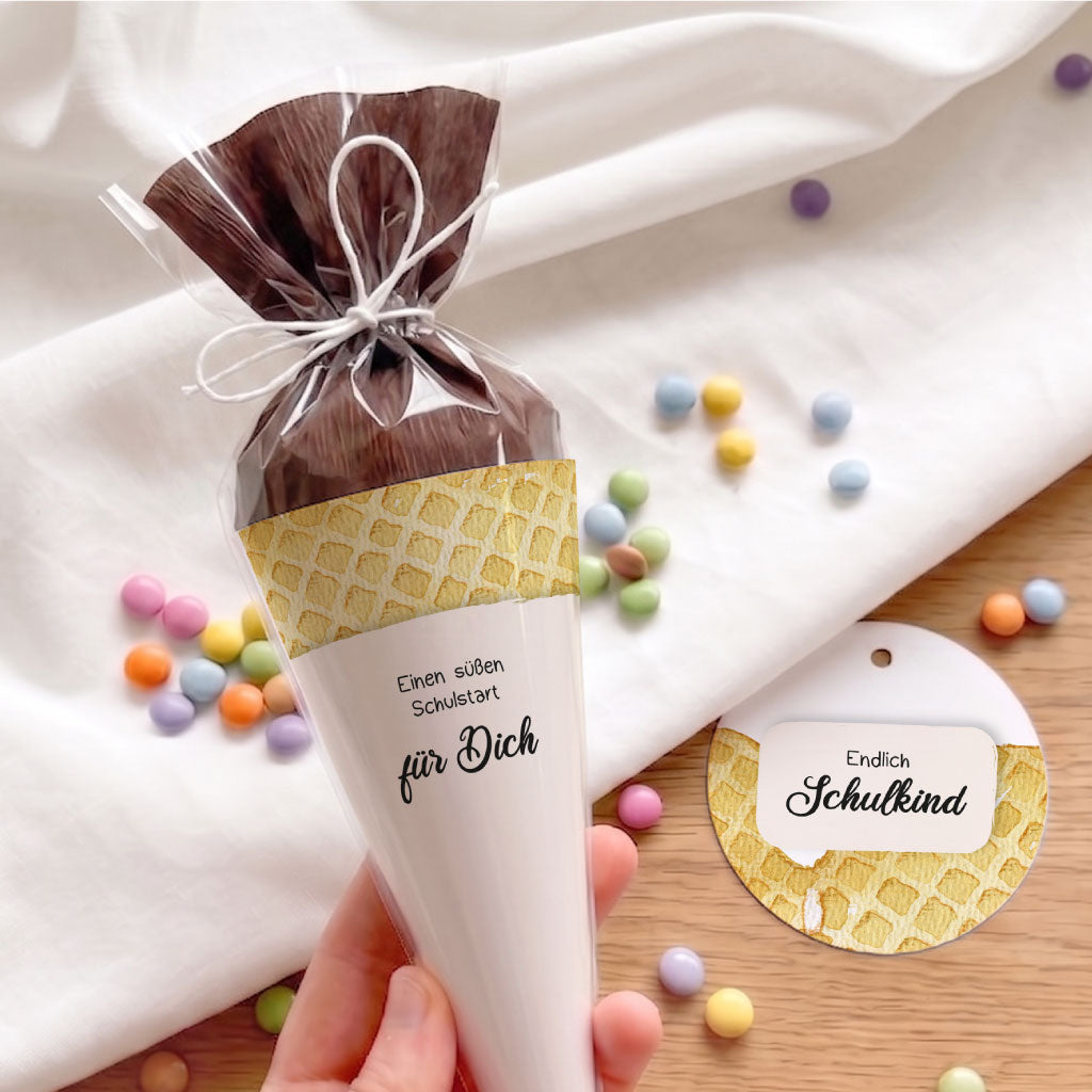 Mini Schultüte mit Waffel Aquarell Motiv neben einem runden Anhänger für das Schulkind und bunten Schokoperlen.