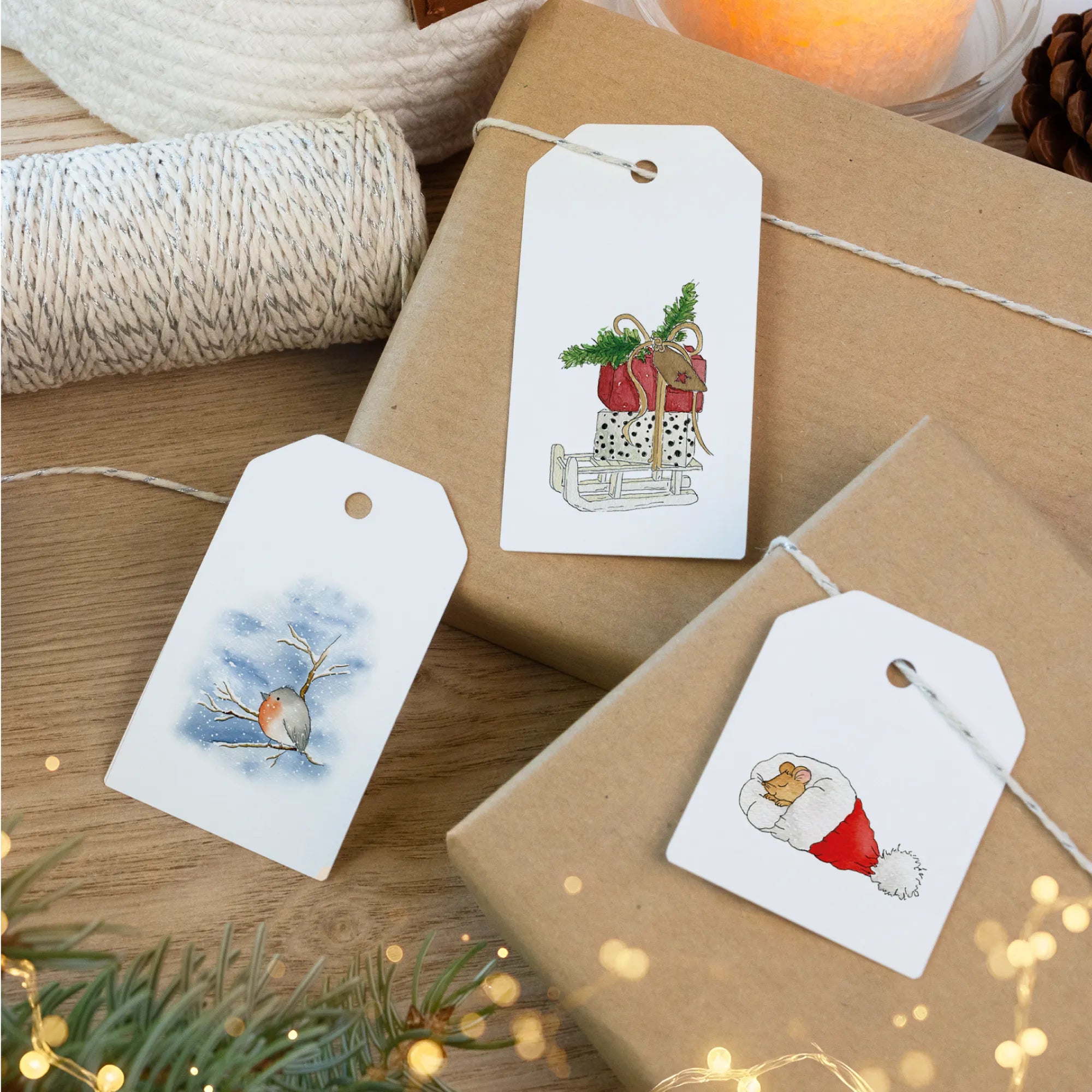 Papieranhänger für Weihnachtsgeschenke zeigen Schlitten mit Paketen, Rotkehlchen auf Ast und schlafende Maus in Weihnachtsmütze.
