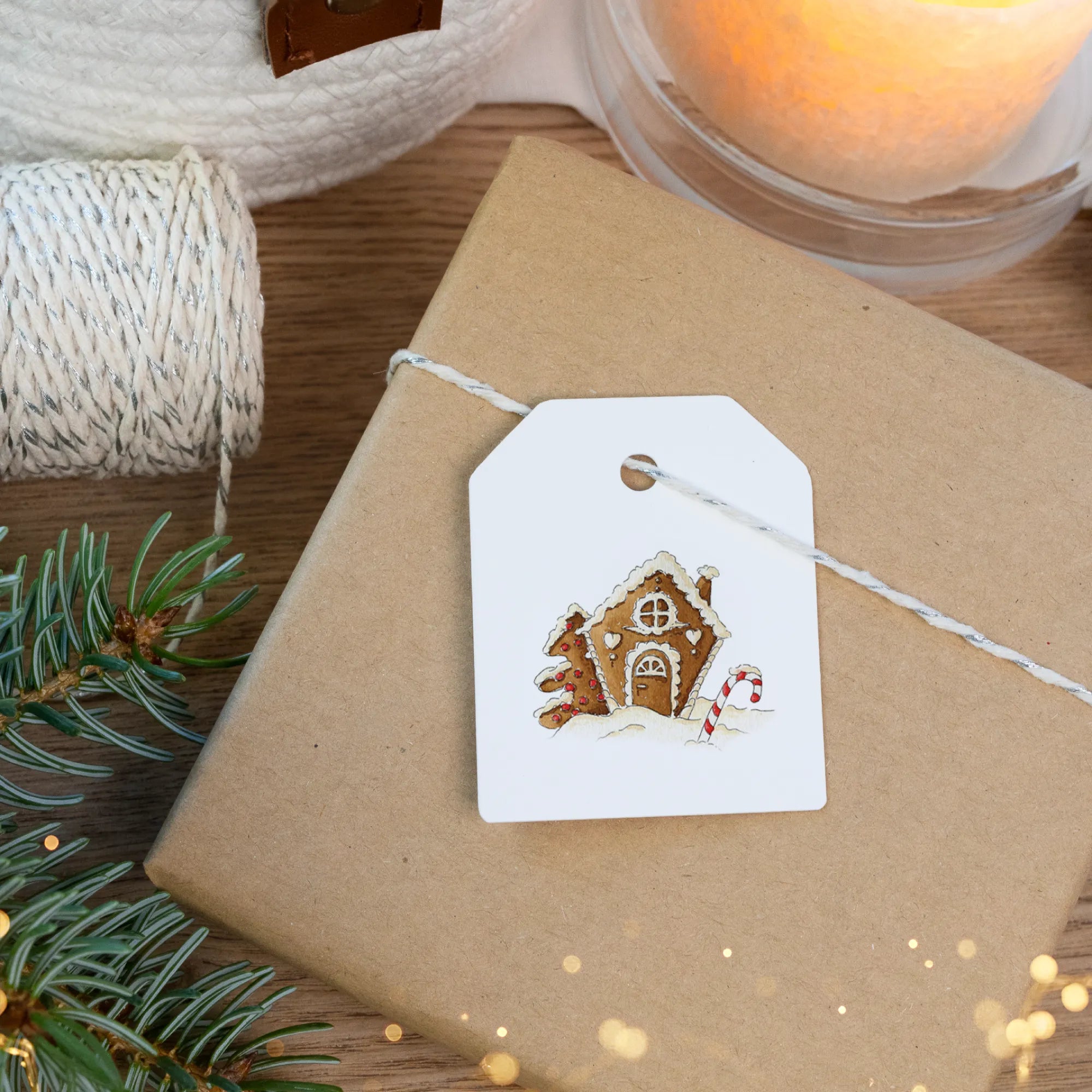 Detailaufnahme eines Geschenkanhängers mit liebevoll gezeichnetem Lebkuchenhaus und Zuckerstange auf weihnachtlichem Paket.
