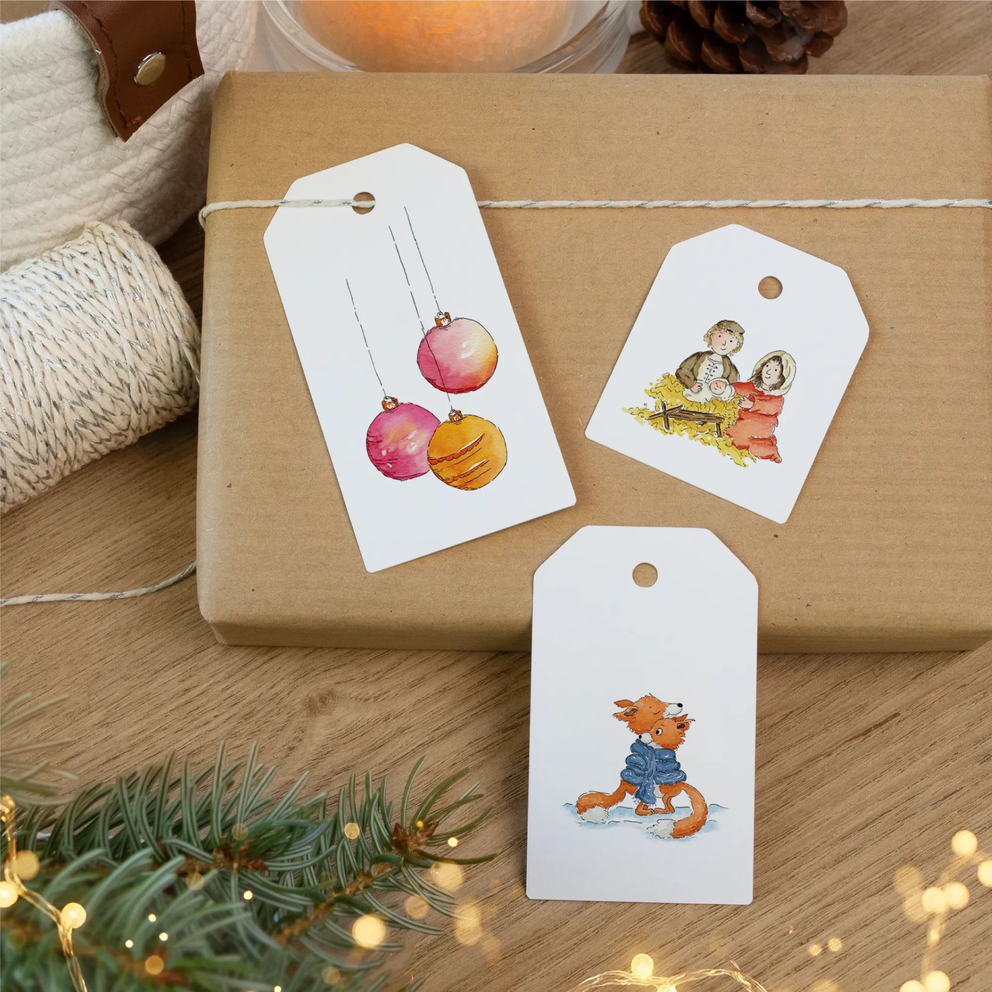 Drei Geschenkanhänger mit bunden Christbaumkugeln, Krippenszene und Füchsen als Dekoration auf einem Weihnachtsgeschenk.