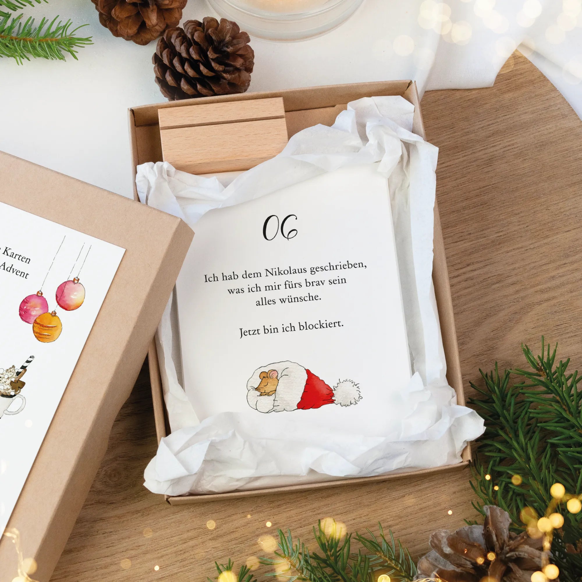 Geöffnete Kraftkarton Schachtel mit Adventskalender Karte 06. Zeigt eine schlafende Maus als Aquarell Motiv in Weihnachtsmütze.