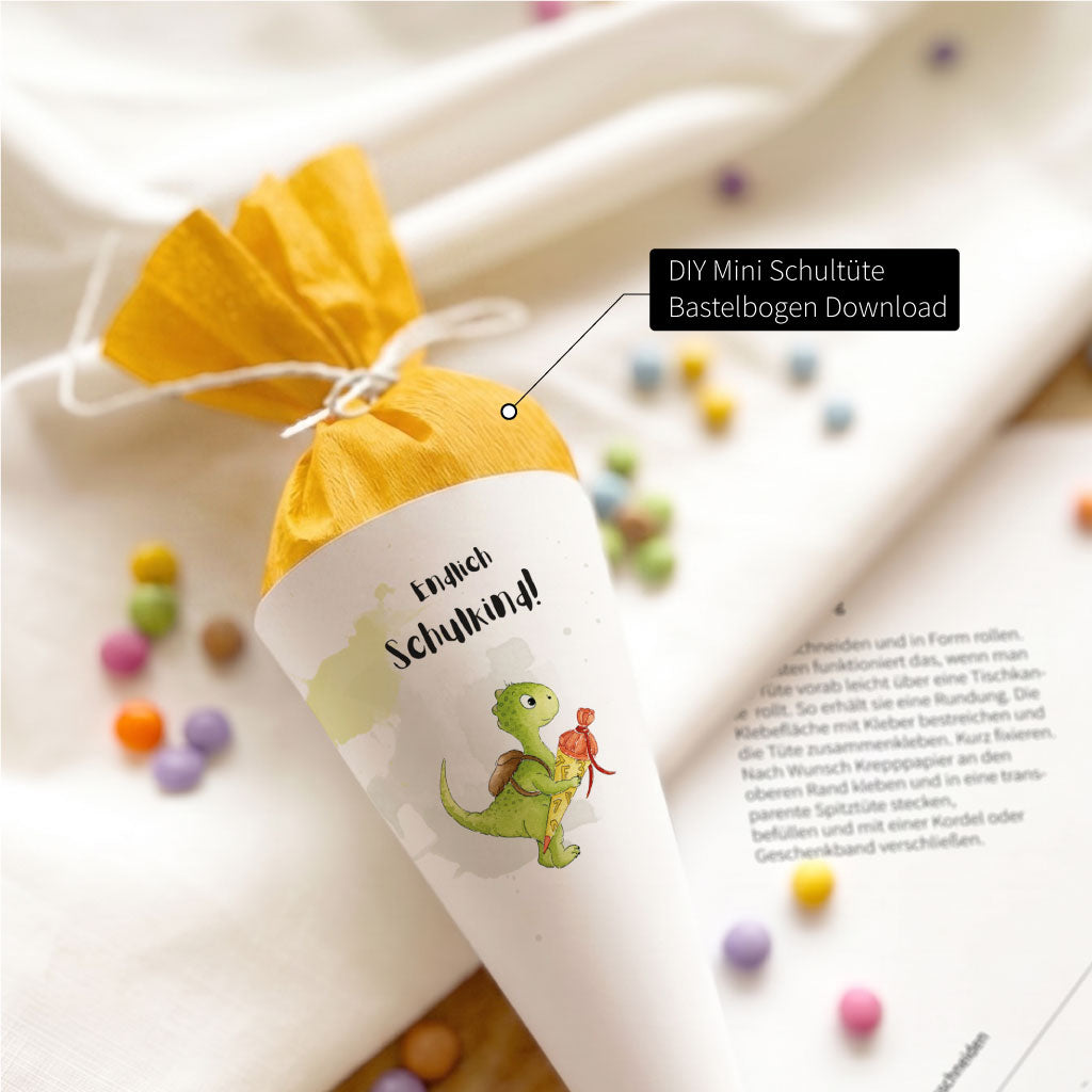 DIY Mini Schultüte mit Dino Motiv und gelbem Krepppapier, gefüllt mit bunten Schokolinsen auf hellem Untergrund.