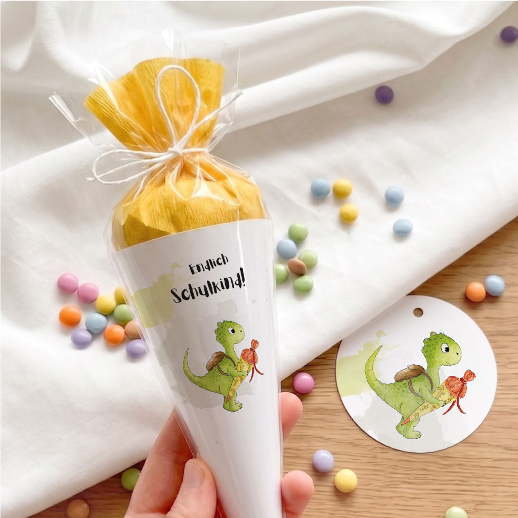 Transparente Spitztüte über der Mini Schultüte mit Dinosaurier Motiv und passendem runden Geschenkanhänger.