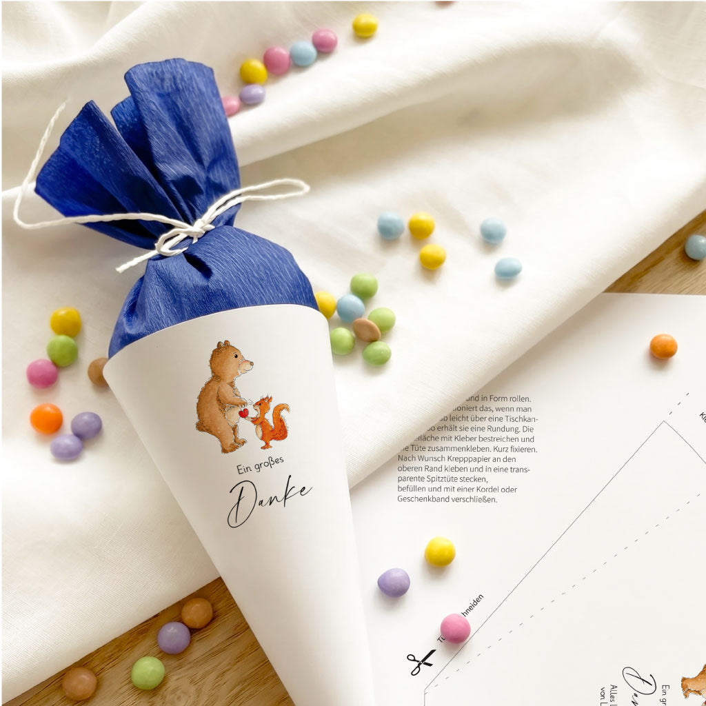 Detailansicht der blauen Mini Schultüte mit Bär und Eichhörnchen Aquarell Motiv neben dem ausgedruckten Bastelbogen.