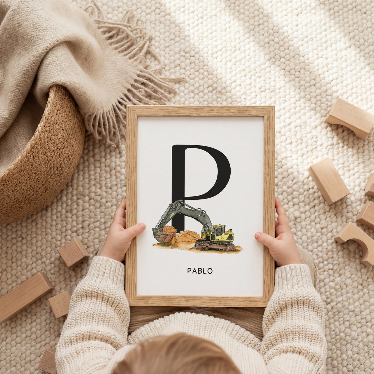 Kind hält personalisierbares Fahrzeugposter mit Aquarell Motiv Bagger, Initiale P und Name Pablo im Holzrahmen in den Händen