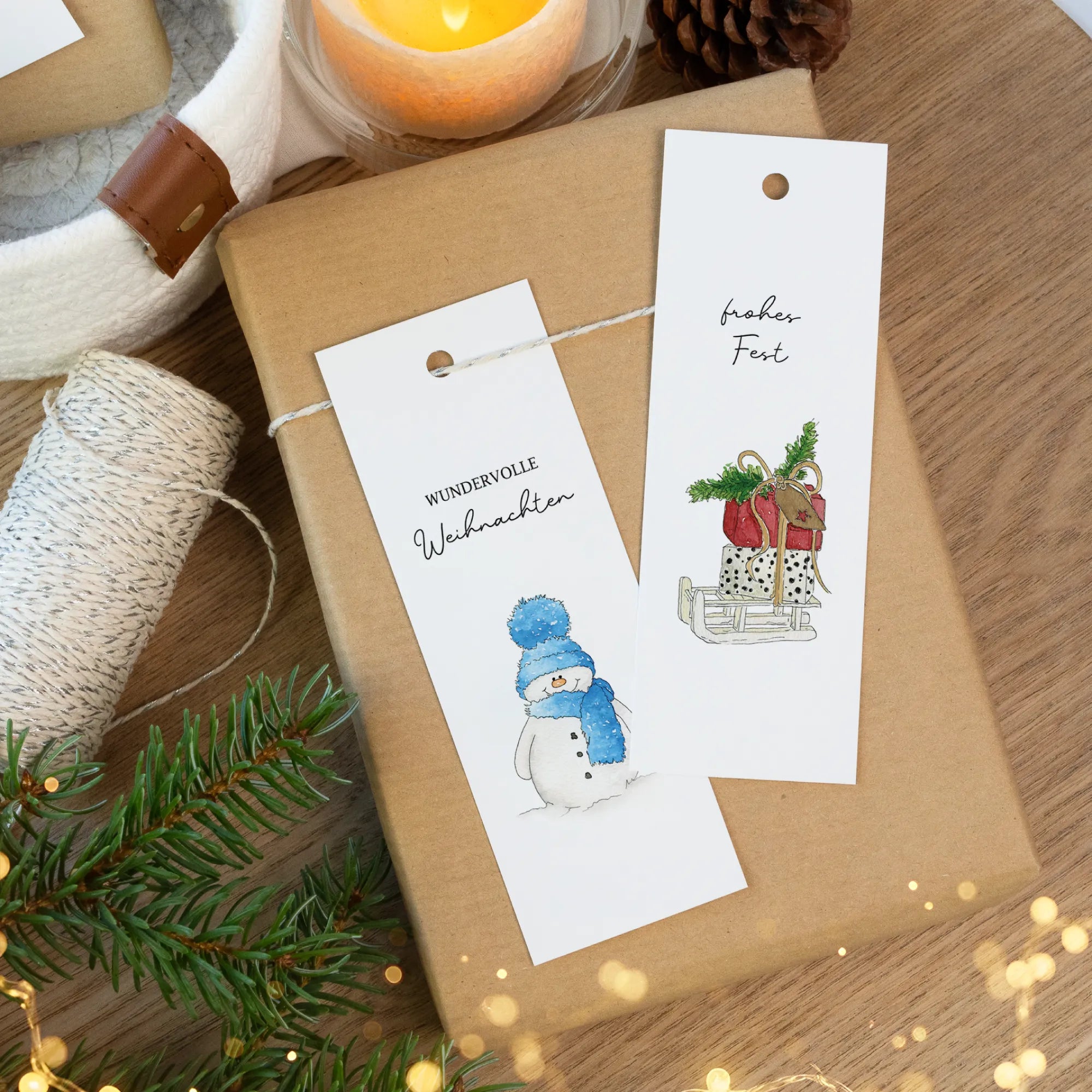 Mehrere weihnachtliche Anhänger mit Aquarell Motiv, drapiert auf einem Paket mit Tannengrün.