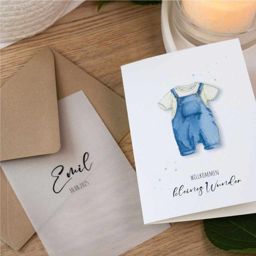 Personalisierte Glückwunschkarte zur Geburt für Jungen mit handgemaltem Aquarellmotiv eines blauen Stramplers und transparentem Deckblatt mit Name und Geburtsdatum.