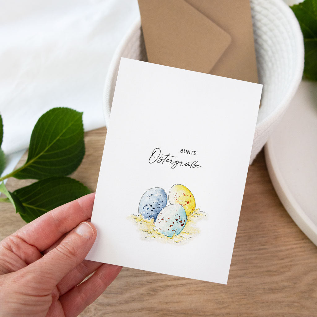 Handgemalte Osterkarte als Klappkarte mit bunten Ostereiern auf Stroh, natürliche Aquarell Postkarte zu Ostern.