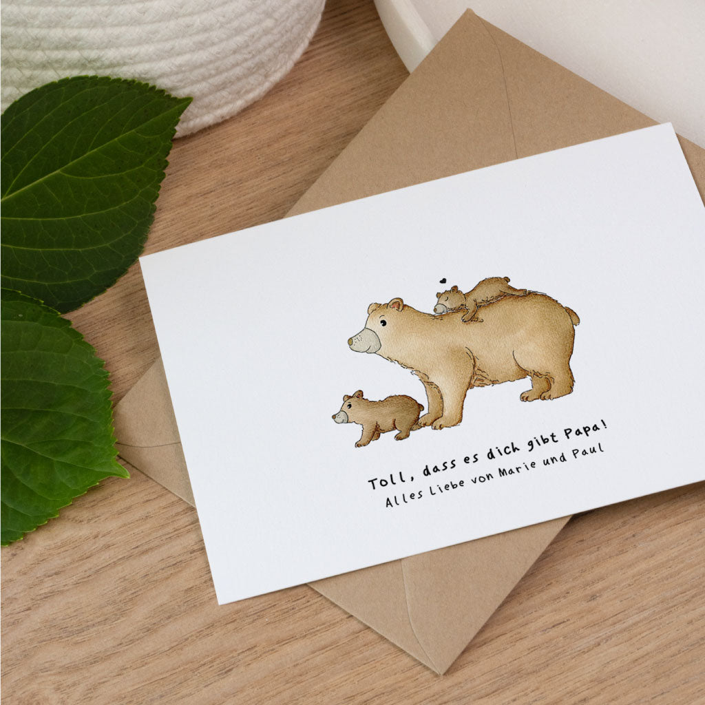 Personalisierbare Glückwunschkarte zum Vatertag mit Bären Aquarell Motiv und Umschlag aus Kraftpapier auf Holztisch.