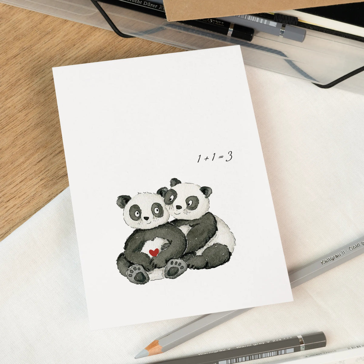Karte zur Schwangerschaftsverkündung mit zwei handgemalten Pandas die sich umarmen, rotes Herz, Schriftzug 1+1=3