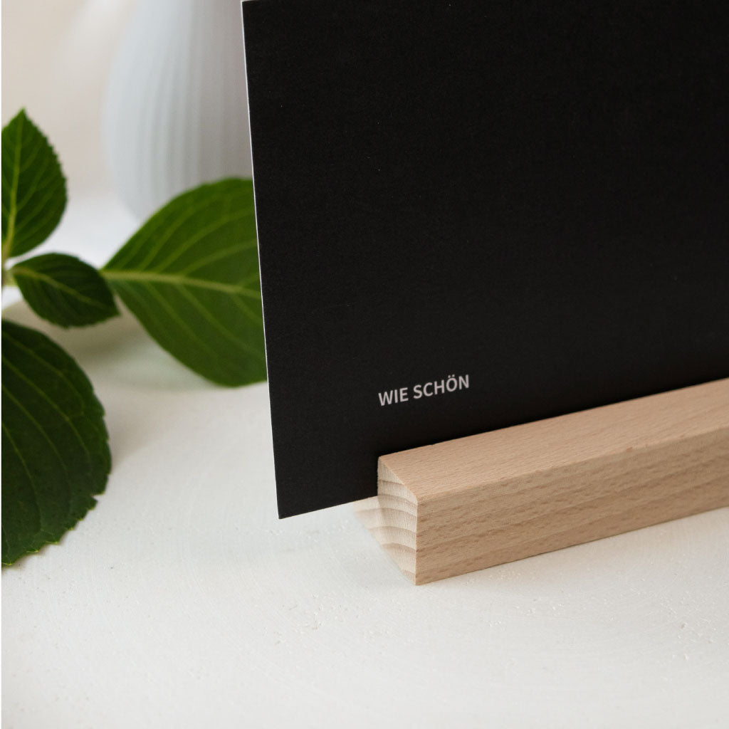 Nahaufnahme: Schwarze Karte steht stabil im Kartenhalter aus Holz – perfekt für Hochzeiten oder als Tischdeko bei einer Feier.