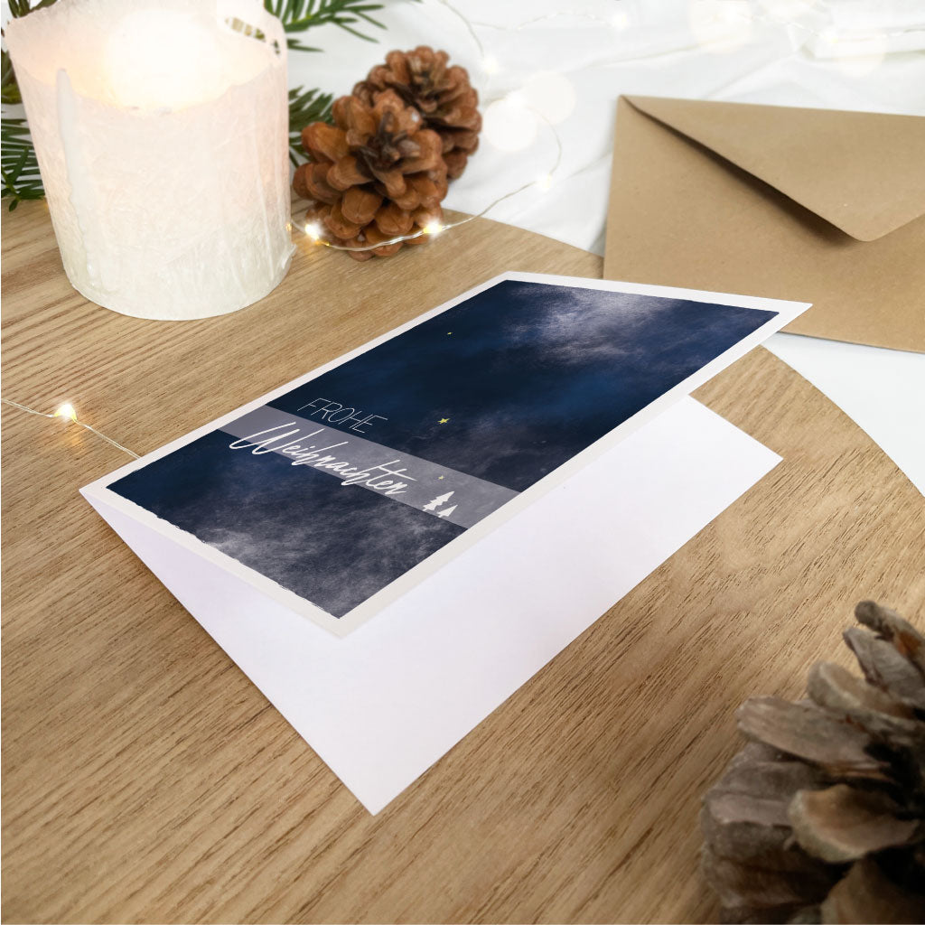 Klappkarte für Weihnachten mit Aquarell Winterhimmel und Text "Frohe Weihnachten", Kuvert aus Kraftpapier im Hintergrund