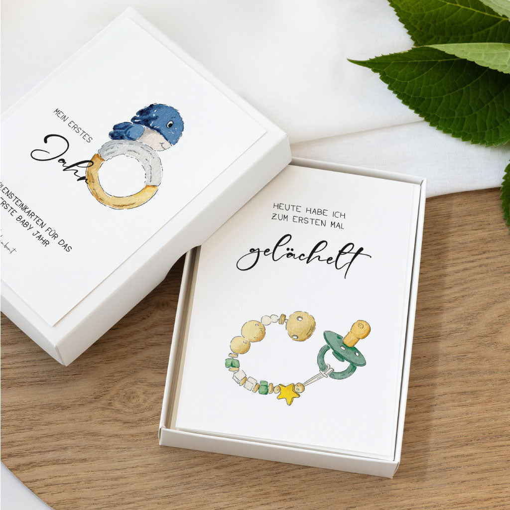 Zwei Babykarten mit handgemalten Aquarellmotiven in geöffneter Geschenkbox, ideal zum Festhalten besonderer Meilensteine im ersten Babyjahr.