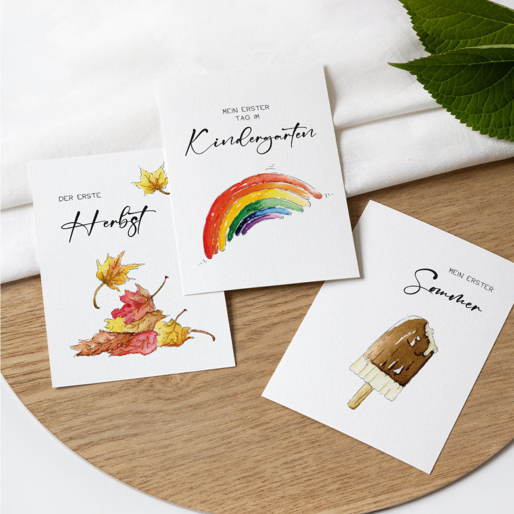 Drei saisonale Meilensteinkarten mit Aquarellmotiven zu Herbst, Sommer und Kindergartenstart – Teil des Sets fürs erste Babyjahr.