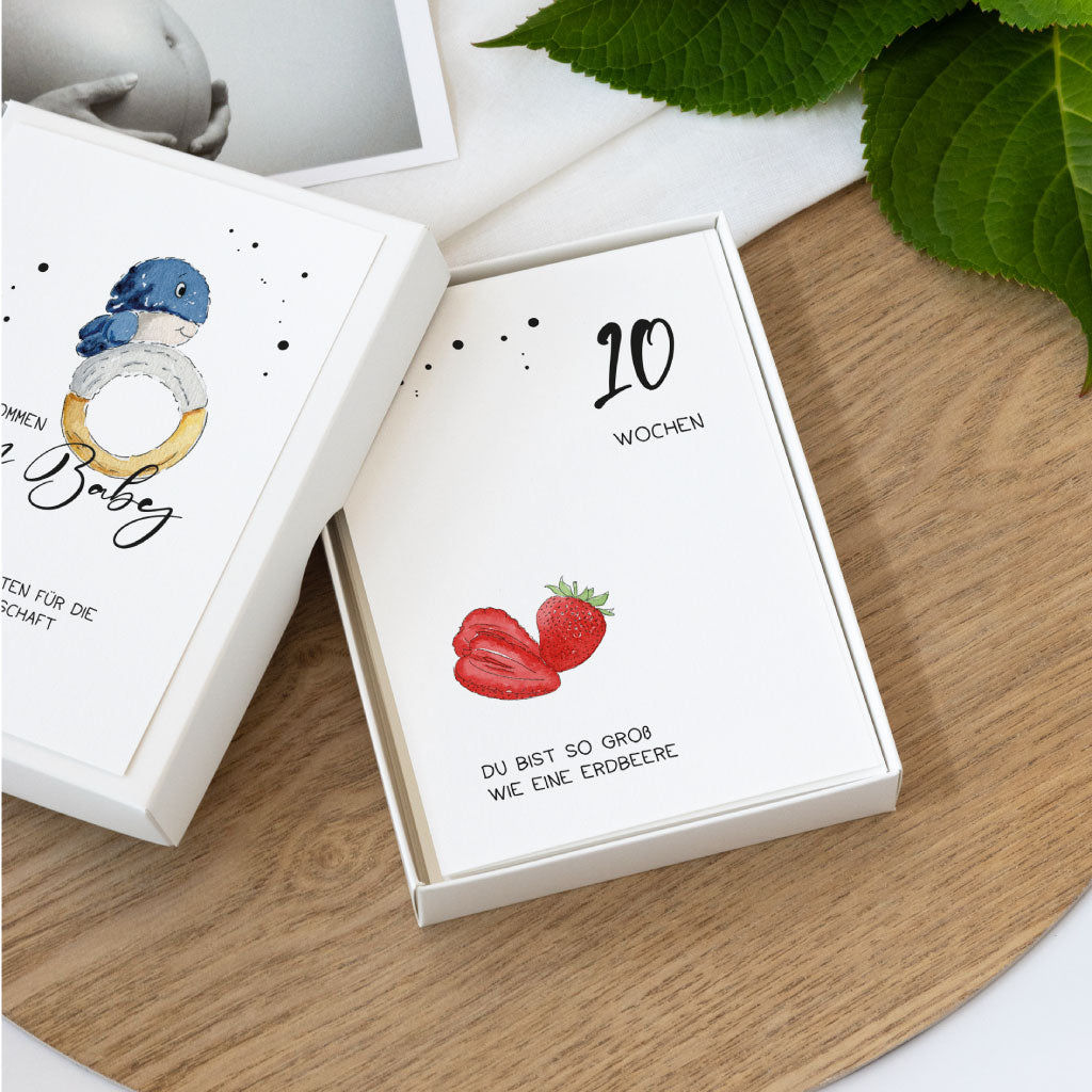 Offene Box mit Schwangerschafts-Meilensteinkarten, sichtbar ist die Karte für die 10. Woche mit Erdbeer-Motiv und handgemaltem Aquarell. Text: „Du bist so groß wie eine Erdbeere“.