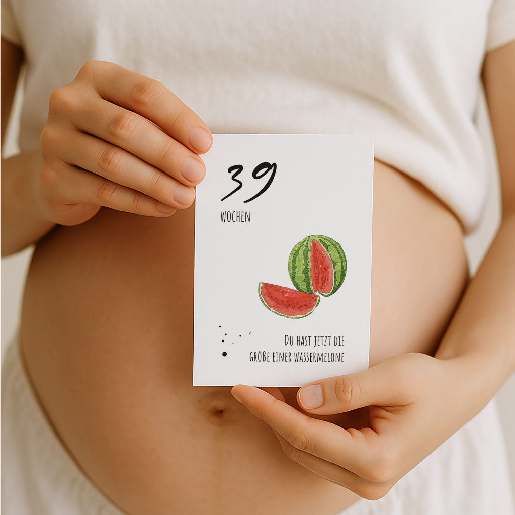Schwangere Frau hält Meilensteinkarte mit Aquarell-Wassermelone zur 39. Schwangerschaftswoche in der Hand. Text: „Du hast jetzt die Größe einer Wassermelone“.