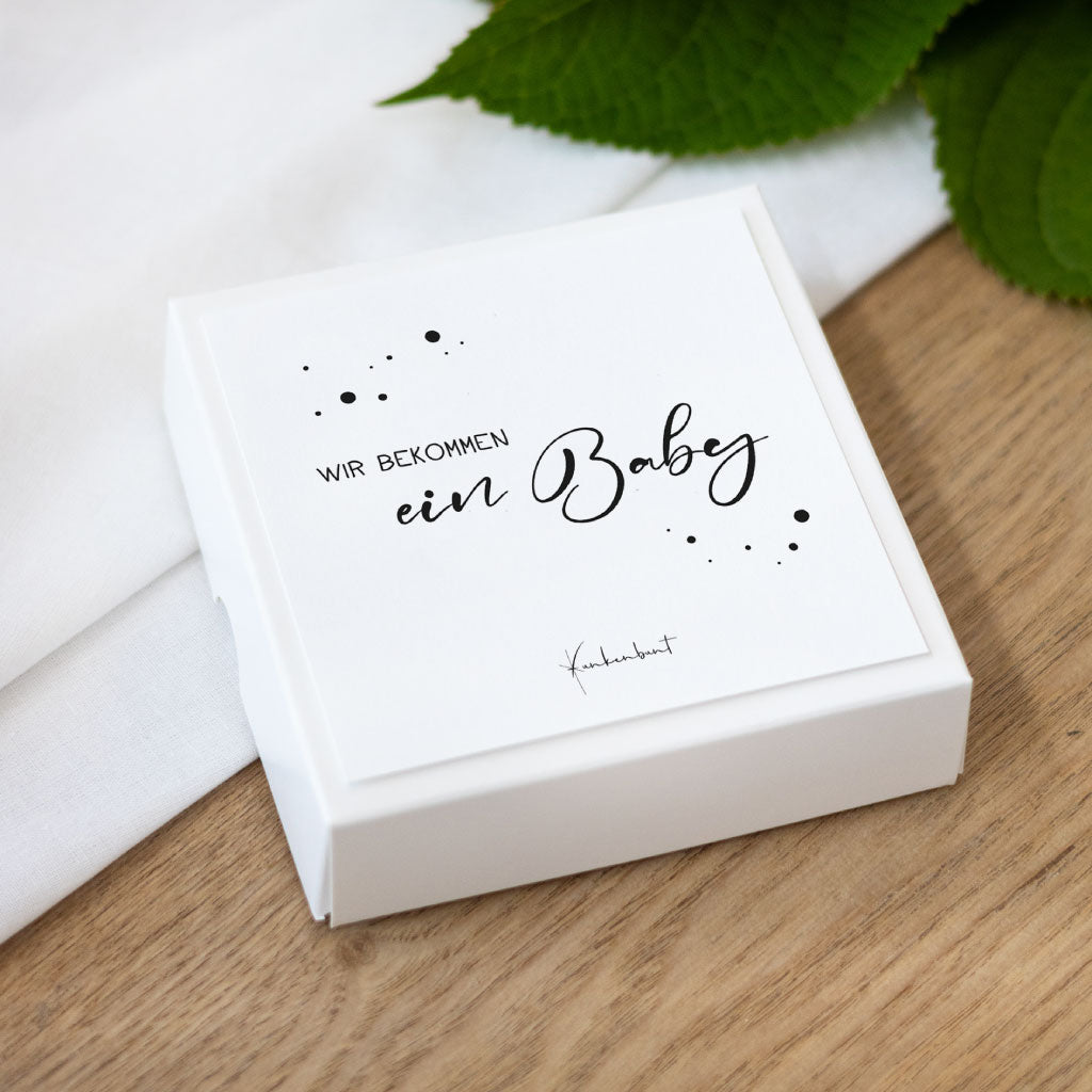Quadratische Box mit der Aufschrift „Wir bekommen ein Baby“, stilvoll verpacktes Set Meilensteinkarten zur Schwangerschaft mit handgemalten Elementen.
