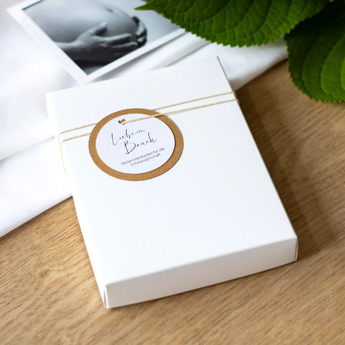 Meilensteinkarten Schwangerschaft als Geschen: weiße  Geschenkbox mit Kraftpapier-Anhänger und der Aufschrift "Liebe im Bauch"